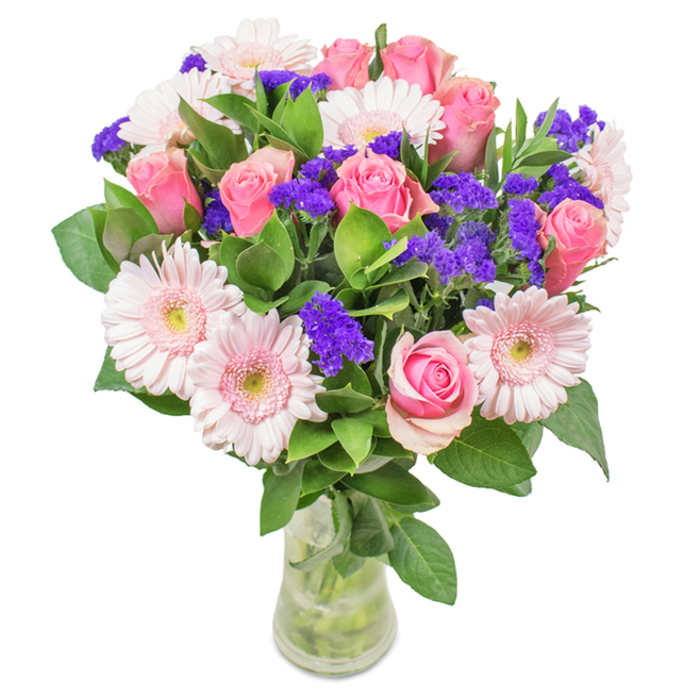 A vibrant, expertly crafted floral arrangement stands in a sleek clear glass vase, its backdrop a pristine white to highlight every nuanced detail. The composition features an artful balance of around 9 pink roses-some tight in bud, others just beginning to unfold in classic spirals-paired with approximately 7 pale pink gerbera daisies, each one boasting a large, open face and delicate, radiating petals with subtle ivory centers. Bright clusters of purple statice punctuate the design, offering vivid contrast and a unique texture akin to the diverse plantings found in Queen Square Garden. Lush, verdant green foliage fills out the bouquet, referencing Bloomsbury's abundant park greenery and infusing the arrangement with energy and depth. The transparent vase subtly reveals the stems and water, grounding the composition in authenticity. Ideal for gifting or display in a refined Bloomsbury townhouse or university office, this bouquet of roses, gerberas, and purple accents conveys warmth, joy, and the spirit of Bloomsbury's artistic heritage.